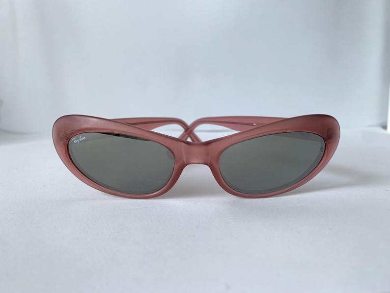 Peut inclure: Lunettes de soleil mauves en forme d'&oelig;il de chat. Les lunettes ont des verres gris fonc&eacute; et le logo Ray-Ban sur la lentille gauche. La monture est de couleur unie et translucide. Sur fond blanc.