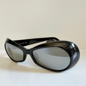May include: Black sunglasses with a curved, wraparound design. The lenses are reflective silver, and the frame is glossy black. The text "B&L RAY-BAN" is visible on the frame. The sunglasses are set against a plain white background.