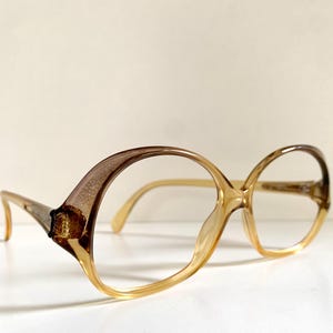 Op de afbeelding: Een paar amberkleurige plastic brillen met een rond, oversized montuur.