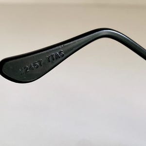 Puede incluir: Primer plano de una punta de varilla de gafas de pl&aacute;stico negro con el texto "#2457 YTAS" impreso en ella.