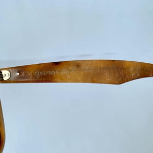 Puede incluir: Primer plano del marco de carey marr&oacute;n de unas gafas de sol Ray-Ban. Las gafas tienen una bisagra de metal dorado y el texto "B&L RAY-BAN USA" est&aacute; grabado en el marco.