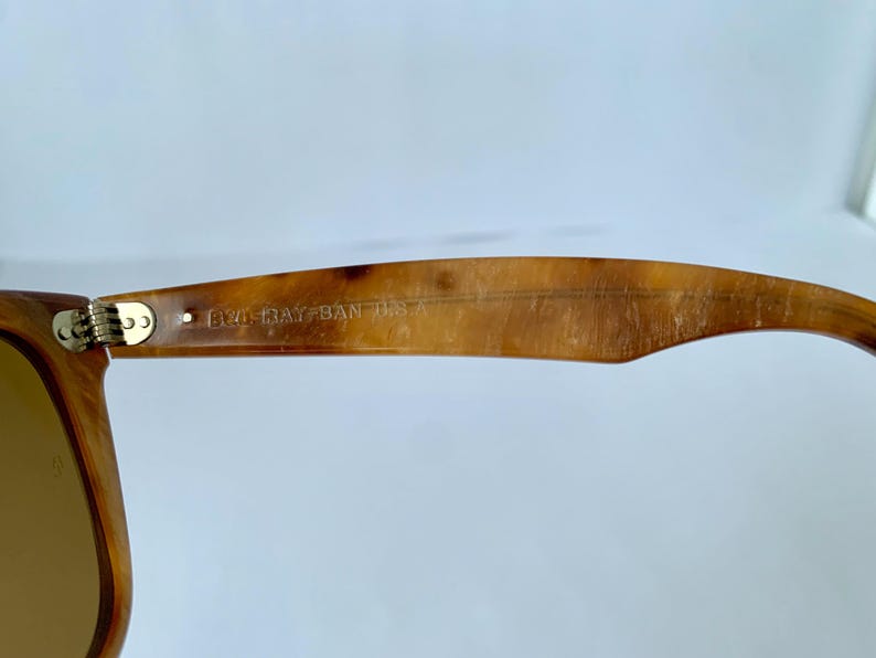 Puede incluir: Primer plano del marco de carey marr&oacute;n de unas gafas de sol Ray-Ban. Las gafas tienen una bisagra de metal dorado y el texto "B&L RAY-BAN USA" est&aacute; grabado en el marco.