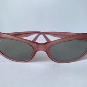 Peut inclure: Lunettes de soleil &oelig;il de chat de couleur mauve avec des verres gris fonc&eacute;. Les lunettes de soleil pr&eacute;sentent un logo Ray-Ban subtil sur la lentille gauche. La monture a une finition mate douce et le design est de style r&eacute;tro classique.