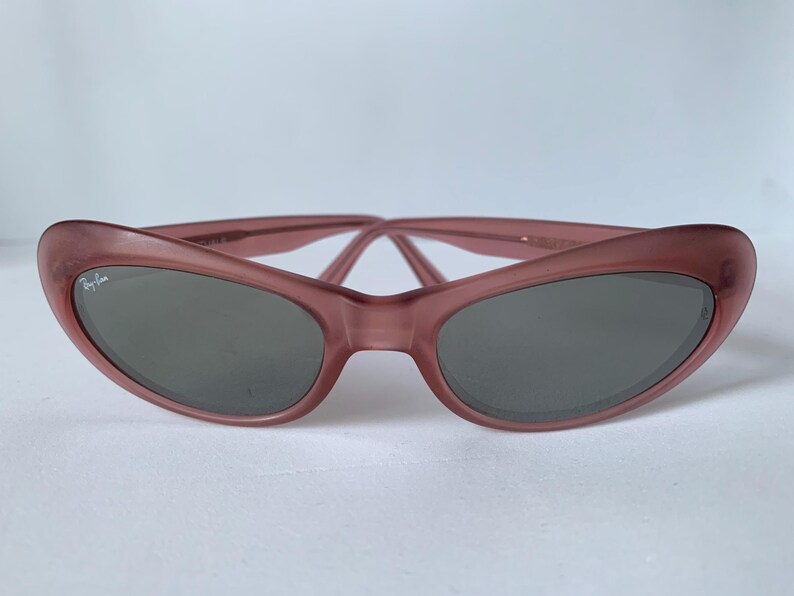 Peut inclure: Lunettes de soleil &oelig;il de chat de couleur mauve avec des verres gris fonc&eacute;. Les lunettes de soleil pr&eacute;sentent un logo Ray-Ban subtil sur la lentille gauche. La monture a une finition mate douce et le design est de style r&eacute;tro classique.
