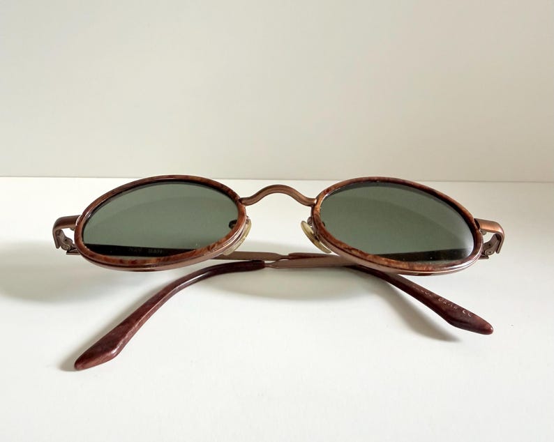 May include: Vintage oval sunglasses with a brown tortoiseshell frame and dark green lenses. The arms are a matching brown colour. The sunglasses are set against a white background.