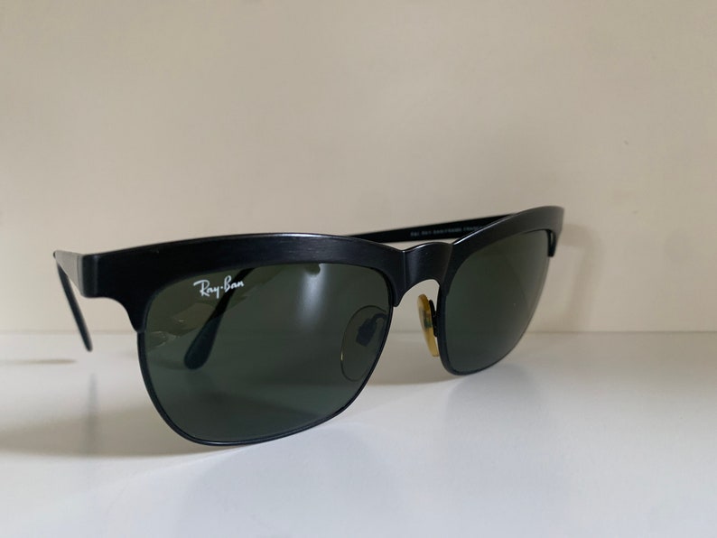 May include: Black Ray-Ban sunglasses with a classic design. The sunglasses have a matte black frame, dark green lenses, and the Ray-Ban logo in white on the left lens. The sunglasses are a timeless accessory.