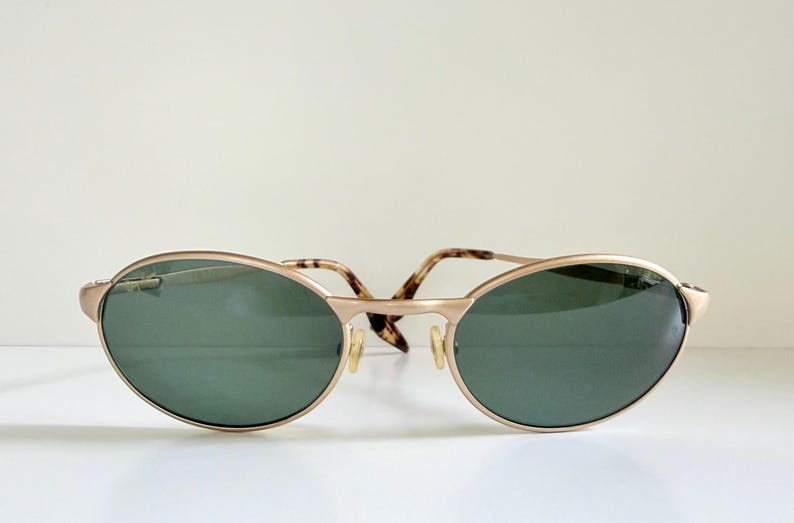 Puede incluir: Gafas de sol ovaladas con montura dorada y lentes verde oscuro. Las patillas presentan un dise&ntilde;o de carey. Un accesorio elegante para la protecci&oacute;n ocular, con un dise&ntilde;o cl&aacute;sico.