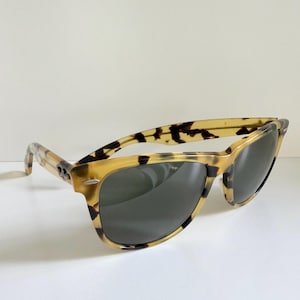 May include: Tortoiseshell sunglasses with dark lenses. The frames have a classic design with a speckled pattern in shades of brown and tan. The sunglasses are angled slightly, showcasing the shape and style.