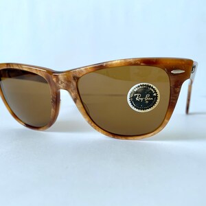 Puede incluir: Gafas de sol Ray-Ban de carey marr&oacute;n con lentes marrones. Las gafas tienen una barra de metal en el puente y una pegatina del logotipo de Ray-Ban en la lente derecha.