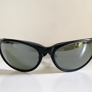 May include: Black sunglasses featuring a wraparound frame design with dark, reflective lenses. The frames are constructed from a smooth, solid black material that curves around the face, providing a wide field of vision and a sleek, continuous look.