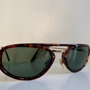 Puede incluir: Gafas de sol aviador de carey con detalles dorados y lentes verdes. Las gafas tienen el logotipo de Ray-Ban en la lente izquierda.