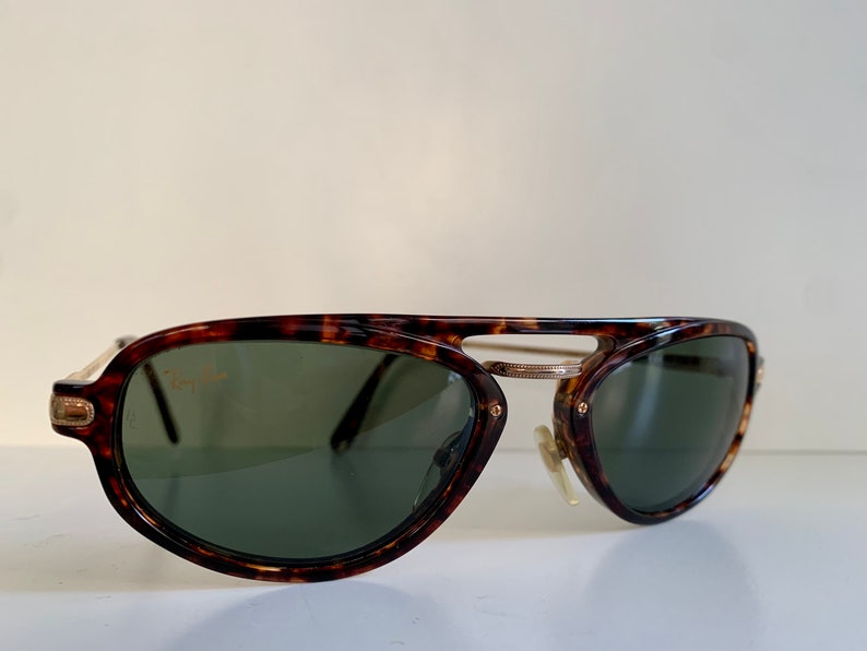 Puede incluir: Gafas de sol aviador de carey con detalles dorados y lentes verdes. Las gafas tienen el logotipo de Ray-Ban en la lente izquierda.