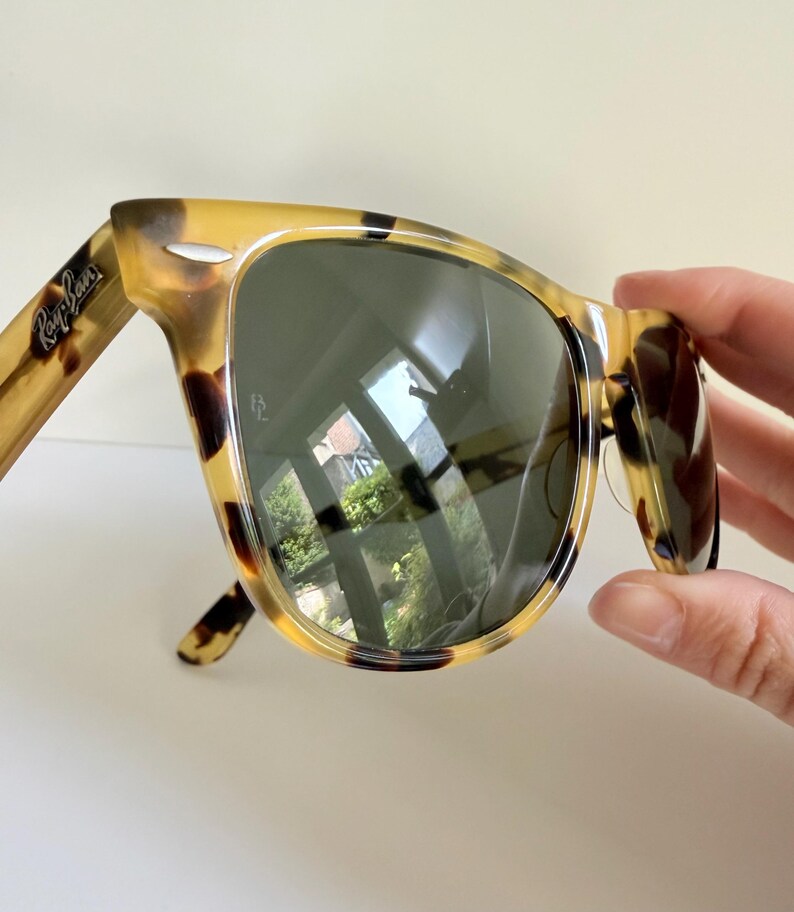 May include: Tortoiseshell-patterned sunglasses with dark lenses. The sunglasses have a classic design with the Ray-Ban logo visible on the temple. The lenses reflect the surrounding environment.