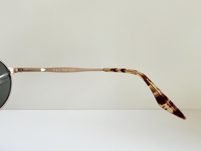 Puede incluir: Primer plano de unas gafas de sol. La montura es de color marr&oacute;n claro, con el texto "B & L RAY-BAN" impreso en la varilla. Las puntas de las varillas tienen un dise&ntilde;o de carey.