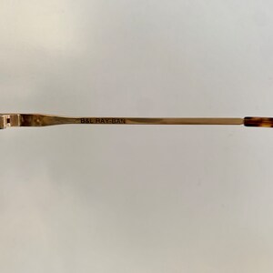 Puede incluir: Primer plano del brazo de metal dorado de unas gafas de sol Ray-Ban de carey. El brazo est&aacute; grabado con el texto "B&L RAY-BAN".
