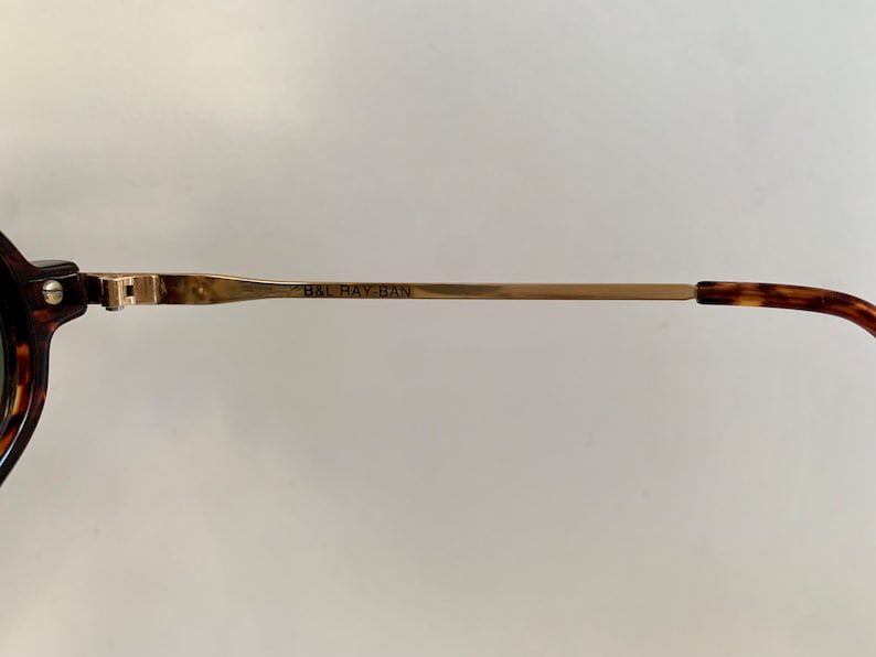 Puede incluir: Primer plano del brazo de metal dorado de unas gafas de sol Ray-Ban de carey. El brazo est&aacute; grabado con el texto "B&L RAY-BAN".