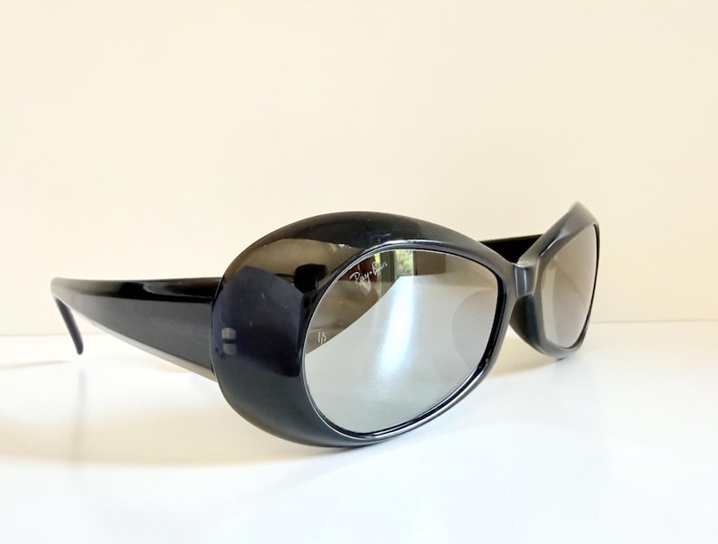May include: Black oversized sunglasses with a glossy finish. The sunglasses have a rounded, oval shape with thick frames and reflective lenses. The arms are sleek and extend back to the temples.