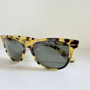 May include: Sunglasses with a classic design. The frames have a tortoise shell pattern in shades of yellow and brown. The lenses are a dark gray color. The sunglasses are set against a white background.