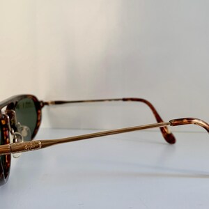 Puede incluir: Gafas de sol con montura de carey, patillas de metal dorado y lentes verdes.