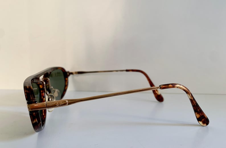 Puede incluir: Gafas de sol con montura de carey, patillas de metal dorado y lentes verdes.