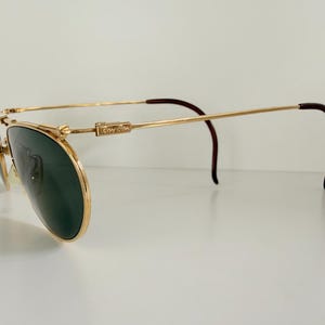 K&ouml;nnte beinhalten: Goldfarbene Ray-Ban Aviator-Sonnenbrille mit dunkelgr&uuml;nen Gl&auml;sern. Die Fassungen haben ein klassisches Doppelsteg-Design und braune B&uuml;gelenden. Das Ray-Ban-Logo ist auf dem B&uuml;gel zu sehen. Ein stilvolles Accessoire zum Schutz der Augen.