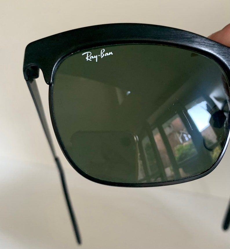May include: Black sunglasses with green lenses. The Ray-Ban logo is visible in white on the upper left of the frame. The sunglasses have a classic design with a thick, dark frame and thin arms.