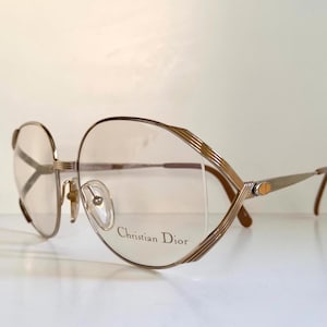Peut inclure: Lunettes Christian Dior vintage avec une monture en métal doré. Les montures ont une forme géométrique unique avec un design strié sur les bords supérieurs. Les verres sont clairs et les branches sont fines avec un détail de logo.