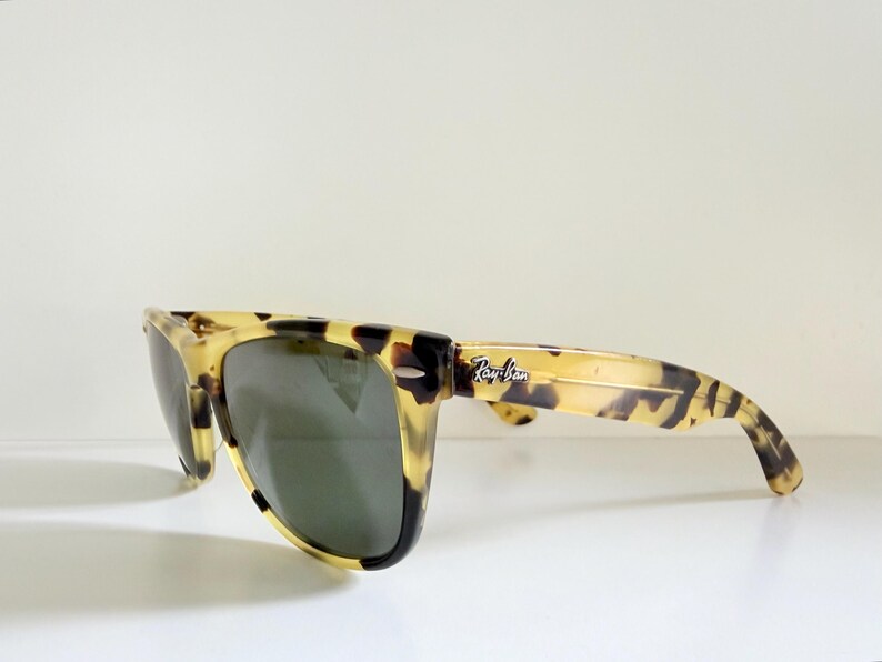 May include: Tortoiseshell-patterned sunglasses with dark lenses. The sunglasses have a classic rectangular frame and the Ray-Ban logo is visible on the temple. The glasses are set against a white background.