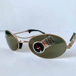 May include: Gold-tone sunglasses with oval lenses and black accents. The sunglasses have a sporty design and a sticker with the text "SPORT" and the Olympic rings.