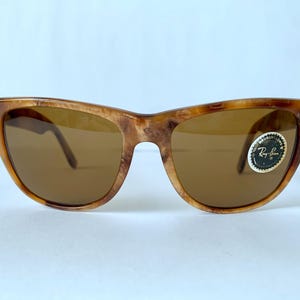 Puede incluir: Gafas de sol Ray-Ban de carey marr&oacute;n con lentes marrones. Las gafas tienen un estilo Wayfarer cl&aacute;sico con una fina barra met&aacute;lica en la parte superior del marco. El logotipo de Ray-Ban es visible en la lente derecha.