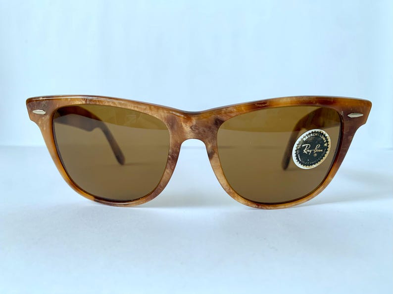 Puede incluir: Gafas de sol Ray-Ban de carey marr&oacute;n con lentes marrones. Las gafas tienen un estilo Wayfarer cl&aacute;sico con una fina barra met&aacute;lica en la parte superior del marco. El logotipo de Ray-Ban es visible en la lente derecha.