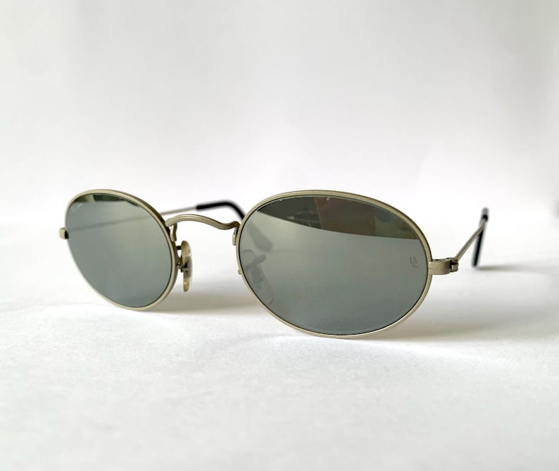 Puede incluir: Gafas de sol ovaladas plateadas con lentes espejados.