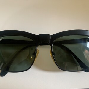 May include: Black sunglasses with a distinctive browline design. The sunglasses feature dark lenses and a matte black frame. The Ray-Ban logo is visible on the upper left lens. The sunglasses have a classic, retro style.