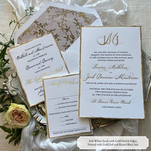May include: Elegant wedding invitation suite with gold foil accents on soft white paper. Includes invitation, RSVP, and details cards, all with deckle edges. The invitation features the couple's initials and event details.