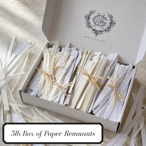May include: A white cardboard box containing bundles of white paper strips tied with tan twine. The inside lid features a black logo with the text Maria Gossard. The box is labeled 5lb Box of Paper Remnants. Loose paper strips surround the box.