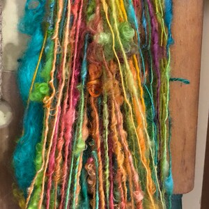 Könnte beinhalten: Eine bunte Garnmischung mit Strähnen in Türkis, Orange, Gelb, Grün und Pink. Das Garn ist in einem lockeren Bündel angeordnet und scheint handgesponnen zu sein.