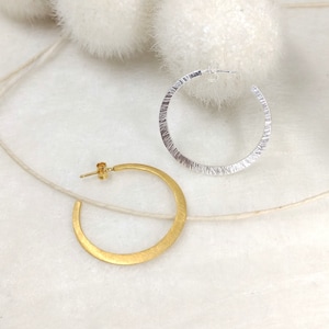 Könnte beinhalten: Ein Paar Creolen, eine golden und eine silberfarben. Beide Ohrringe haben eine strukturierte Oberfläche.