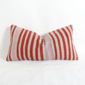 Peut inclure: Un coussin lombaire rectangulaire présentant un motif tissé de rayures verticales alternant des tons de rouge vif, de vert menthe pâle et de rose tendre. Le textile a un aspect tissé à la main avec des lignes verticales régulières sur la surface.