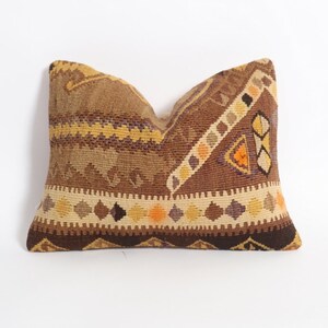 May include: A brown, yellow, and orange patterned throw pillow with a geometric design. The pillow is made of woven fabric and has a fringed edge.