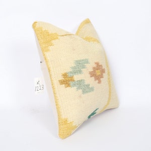 May include: Cream-coloured decorative cushion with geometric patterns in gold, light blue, and peach. The cushion has a textured surface and a solid cream-coloured back. The tag reads "K 1223".