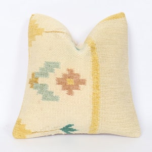 May include: Cream-coloured decorative cushion with a woven texture. The cushion features a central design with a floral motif in shades of brown, blue, and yellow. Yellow stripes border the cushion's edges, adding colour to the neutral base.