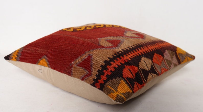 May include: A red, orange, brown, and beige patterned throw pillow with a white cotton backing.