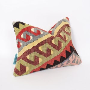 May include: A colorful, geometric patterned pillow with a red, green, yellow, and blue design. The pillow is made of woven fabric and has a fringed edge.