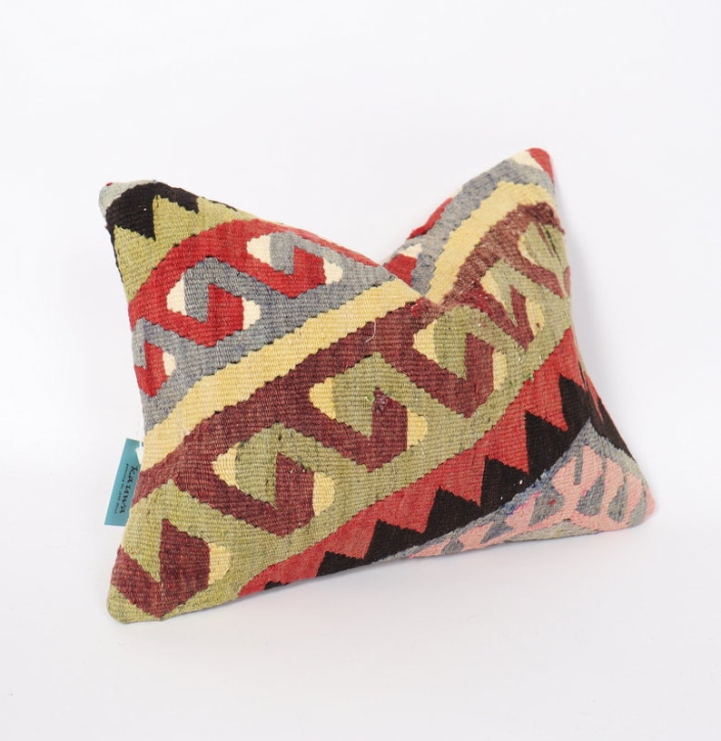 May include: A colorful, geometric patterned pillow with a red, green, yellow, and blue design. The pillow is made of woven fabric and has a fringed edge.