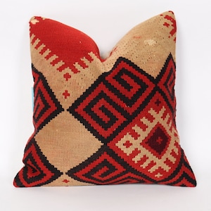 Puede incluir: Una almohada de tiro roja, beige y negra con un diseño geométrico. La almohada está hecha de tela tejida y tiene un aspecto tradicional.