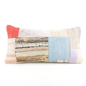 May include: A patchwork pillow with a variety of colors and textures, including red, white, blue, and brown. The pillow is made from different fabrics and has a rectangular shape.