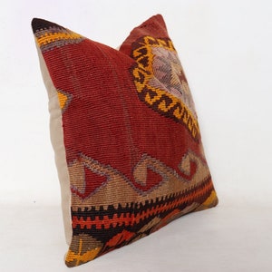 May include: A red, orange, and brown patterned throw pillow with a beige backing. The pillow is made from a woven fabric with a traditional design.