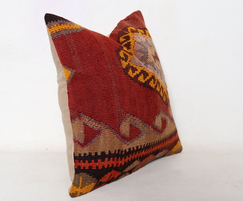 May include: A red, orange, and brown patterned throw pillow with a beige backing. The pillow is made from a woven fabric with a traditional design.