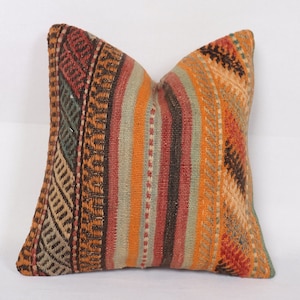 May include: A square throw pillow with a colourful striped pattern in shades of orange, red, brown, green, and beige. The pillow is made of woven fabric with a textured surface.