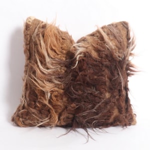 May include: A brown and white fluffy pillow with a shaggy texture. The pillow is made of natural fibers and has a rustic look.